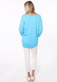 Maglietta azzurro chiaro a maniche lunghe con scollatura rotonda e orlo sfilacciato, abbinata a pantaloni bianchi arrotolati e espadrillas color nocciola.