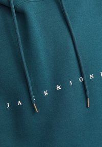 Teal hettegenser med hvit "JACK & JONES" logo, med snøring med metallender og et glatt, teksturert stoff.