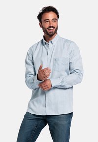 Lichtblauw overhemdd met een borstzak, gemaakt van een zachte, textuurstof. Gecombineerd met donkerblauwe jeans.