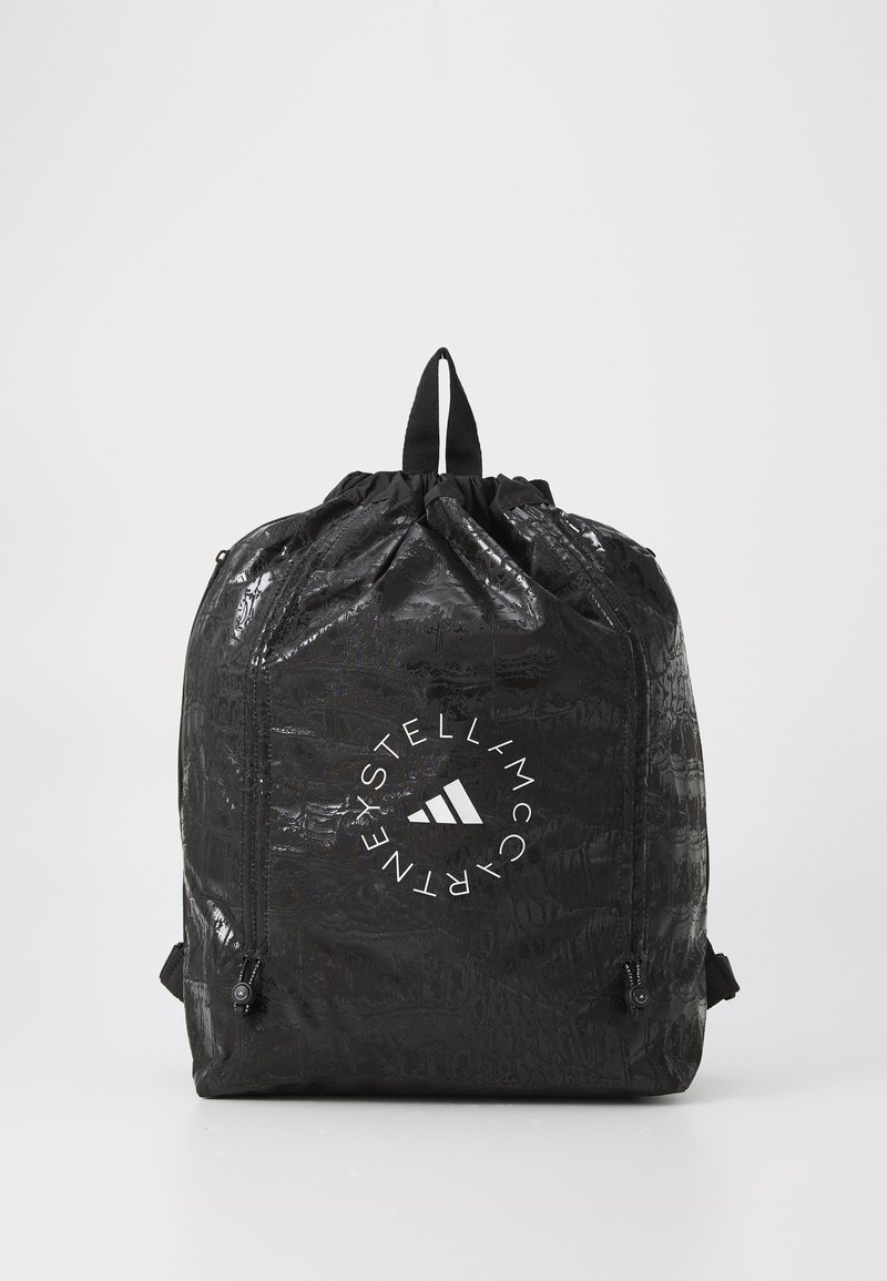 Must kärgiga seljakott krokodillimustriga, millel on silmapaistev valge ümmargune logo, millel on kolm diagonaalset riba. Sisaldab ülemist käepidet.