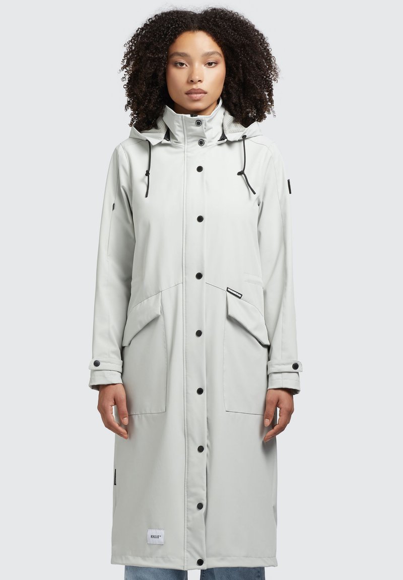 Impermeable de color gris claro con capucha, botones negros, dos grandes bolsillos frontales y un cordón ajustable en el cuello.