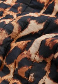 Tissu matelassé avec un motif léopard noir, marron et beige, présentant des coutures visibles et une texture légèrement froissée.