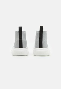 Ein Paar graue Strick-Ankle-Sneaker mit schwarzen Fersenlaschen und dicken weißen Sohlen, die hinten mit "Moschino" geprägt sind.
