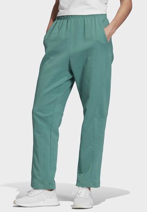 Personne portant un pantalon ample vert sarcelle avec une taille élastique et des poches, associé à des baskets blanches et un haut blanc.