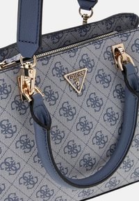 Sac fourre-tout bleu et gris avec un motif de logo entrelacé, une quincaillerie dorée, deux poignées supérieures et une bandoulière amovible.