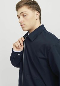 Námornícky modrá bunda vyrobená z hladkej látky, s uzáverom na zips, širokým golierom a prednými vreckami; ležérny strih s štruktúrovaným tvarom.