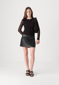 Svart langermet topp med røde prikker, parret med et svart skinn miniskjørt med sølv nagler. Svart slingback sandaler og vevd veske.