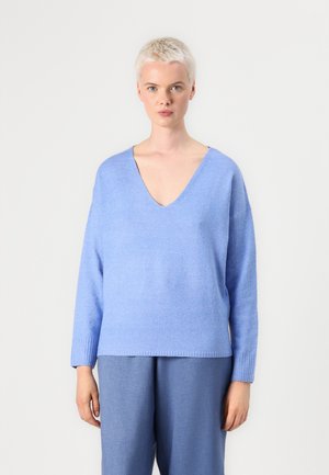 Helles blaues Strickpullover mit tiefem V-Ausschnitt, überschnittenen Schultern, langen Ärmeln und geripptem Saum. Weiche Textur. Kombiniert mit passenden blauen Hosen.