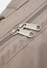 Twee zilveren ritsen met de gravure "anello" op beige textuur stof, weergegeven in close-up detail.