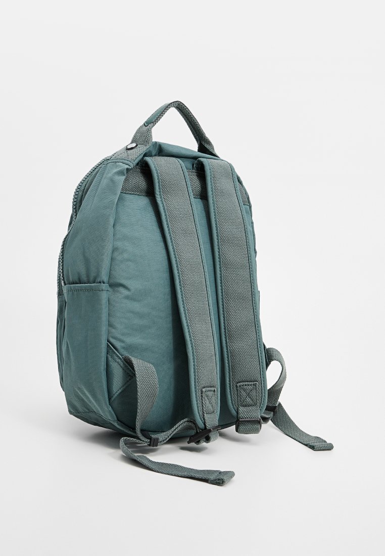 Mochila de tela en color azul verdoso con correas de hombro acolchadas, lados texturizados y un asa superior. Cuenta con dos bolsillos laterales y un cierre de cremallera.