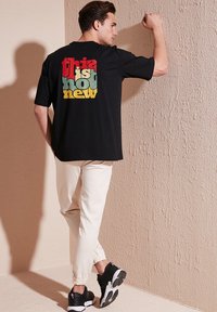 Černé tričko s vícebarevným textem na zádech, které říká "tohle je horká novinka". V kombinaci s krémovými tepláky a černými teniskami.