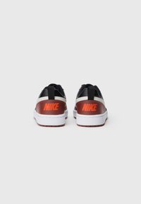 Nike sko med svart mesh-overdel, hvit såle og kontrasterende røde og brune detaljer, med stort logo på hælen.