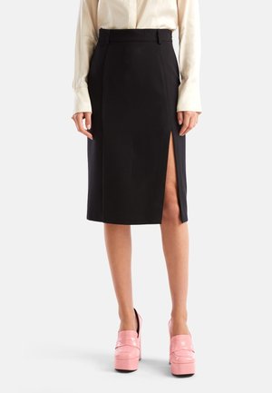 Jupe crayon noire avec une taille haute et une fente frontale. Tissu lisse, design ajusté et passants de ceinture. Portée avec des chaussures à plateforme roses.