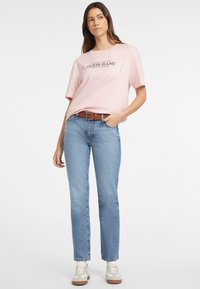Heled pokaaluga roosa lühikeste varrukatega T-särk, millel on must "Guess Jeans" logo, millele on lisatud keskmiselt pesu saanud sirged teksad ja valged tossud pruuni aktsendiga.