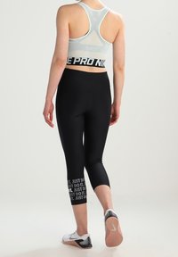 Leggings capri noirs avec le texte "JUST DO IT." sur la jambe gauche, assortis à un soutien-gorge de sport bleu clair à dos nageur avec une bande noire.