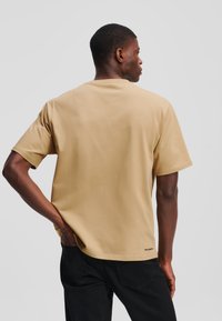 Lühikeste varrukatega, ümmarguse kaelusega t-särk heleses klassikalises puuvillas. Lõdva lõikega, nähtava brändi sildiga hemil ja sujuva tekstuuriga.