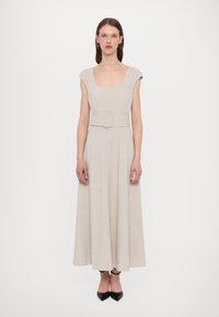 Snygg klänning i golvlång modell i ett ljusbeige tyg, med fyrkantig halsringning och breda axelremmar, åtdragen vid midjan med ett bälte.