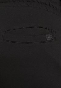 Sorte stretchstofbukser med en synlig baglomme, mærkat med teksten "CARS JEANS" og en glat, tekstureret finish.