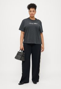 Szara koszulka z logo "Tommy Hilfiger" w stylu pisma, połączona z czarnymi spodniami typu wide-leg z białymi paskami po bokach oraz małą czarną torebką.