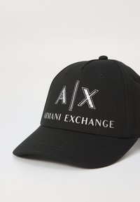 Juodas beisbolo kepurė, pagaminta iš medvilnės, su kreiva vizorė. Priekyje yra sidabrinė siuvinėta "A/X" logotipas ir tekstas "ARMANI EXCHANGE".