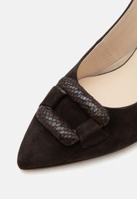 Gros plan d'une chaussure en daim marron foncé à bout pointu avec une boucle rectangulaire texturée à motif serpent sur le dessus.