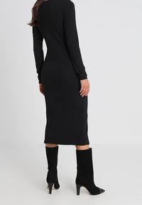 Svart ribbat stickat klänning med lång ärm, knälång, åtsittande design. Bärs med svarta mocka ankelstövlar och spetsiga klackar.