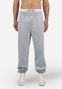 Grijze joggingbroek met een elastische tailleband, voorzien van een wit logo en boorden. De stof heeft een zachte textuur, geschikt voor casual kleding.