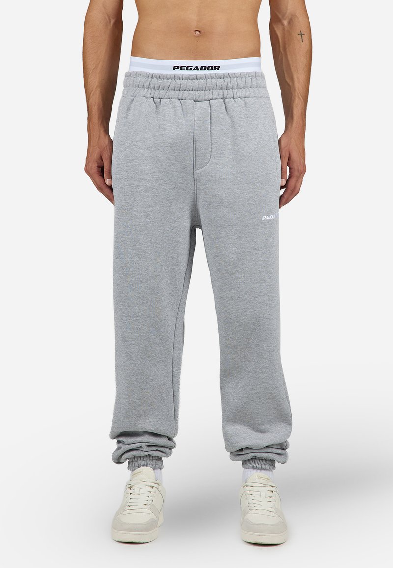 Grijze joggingbroek met een elastische tailleband, voorzien van een wit logo en boorden. De stof heeft een zachte textuur, geschikt voor casual kleding.