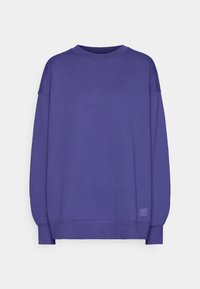 Sudadera morada de tela suave, con cuello redondo, hombros caídos y puños acanalados. Incluye un pequeño parche con el logo en el dobladillo.