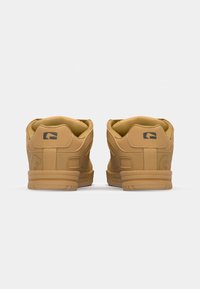 Brown sneakers with a smooth matte finish, rounded toe, padded collar, and logo accents on the back. Flat rubber outsole and cushioned insole.