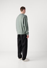 Světle zelený ribbed pletený svetr, volného střihu, kombinovaný s černými širokými kalhotami a bílými teniskami, pohled zezadu.