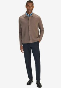 Bruine button-up cardigan met een platte kraag, van textuurlijke brei stof, gecombineerd met een lichtblauw shirt en donkere broeken, gedragen met zwarte schoenen.