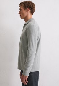 Hellgraues Langarm-Polohemd mit Kragen, figurbetontem Design und weicher Textur, getragen mit dunklen Hosen, seitlich präsentiert.