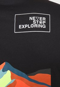 Camiseta negra con un diseño de montaña colorido en azul, verde, naranja y rojo, con texto en blanco que dice "NUNCA DEJES DE EXPLORAR."