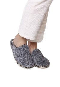 Pantofole grigie e morbide, realizzate in un materiale soffice, con punta rotonda, design slip-on e un bordo decorato lungo la suola. Indossate con pantaloni color crema.