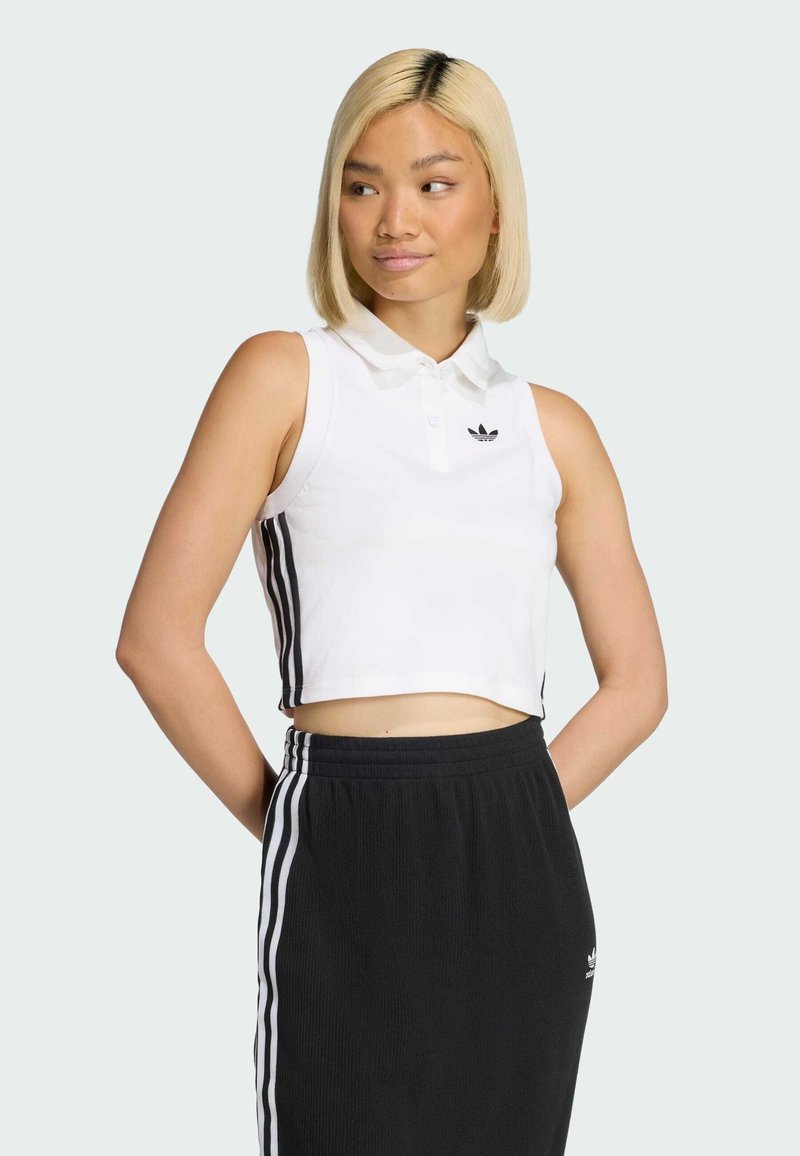 Biała krótka koszulka polo z kołnierzykiem i czarnym logo Adidas, w połączeniu z czarną spódnicą z białymi paskami po bokach. Gładkie tekstury tkaniny.