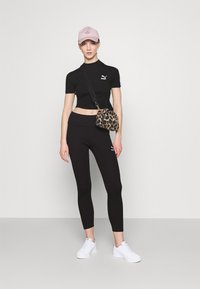 Melnā krūšautā blūze un legingi ar Puma logo, apvienoti ar baltām sporta apaviem un leopardu raksta somu. Rozā cepure papildina tēlu.