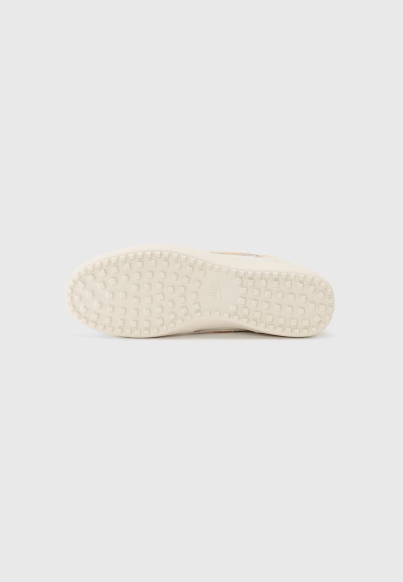 Baskets avec une semelle extérieure en caoutchouc beige texturé, comportant de petites motifs carrés et un logo de marque visible. Design épuré et minimaliste.