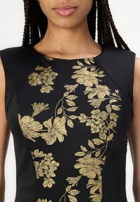 Rochie neagră cu un model floral auriu, decolteu solid și design fără mâneci. Materialul pare neted, având o siluetă ajustată.