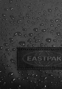 Czarna tkanina o teksturowanej powierzchni, z kroplami wody i wytłoczonym logo "EASTPAK" na dole.