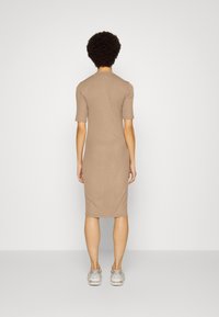 Vestido justo de jersey bege com mangas curtas, até ao joelho, design minimalista, textura suave, usado com sapatilhas de cor clara.