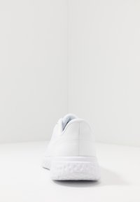 Zapatilla deportiva blanca, con parte superior de malla, tacón redondeado, media suela texturizada, acabado suave, diseño minimalista sin logotipos ni patrones visibles.