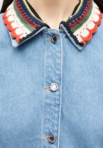 Τζιν μπουφάν με πολύχρωμο κεντητό γιακά σε κόκκινο, λευκό, πράσινο, μπλε, κίτρινο και μαύρο, με ασημί κουμπιά κουμπώματος εμπρός.