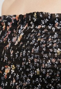 Black floral top featuring a smocked design with ruffled neckline, adorned with small multicolored flowers and textured fabric.