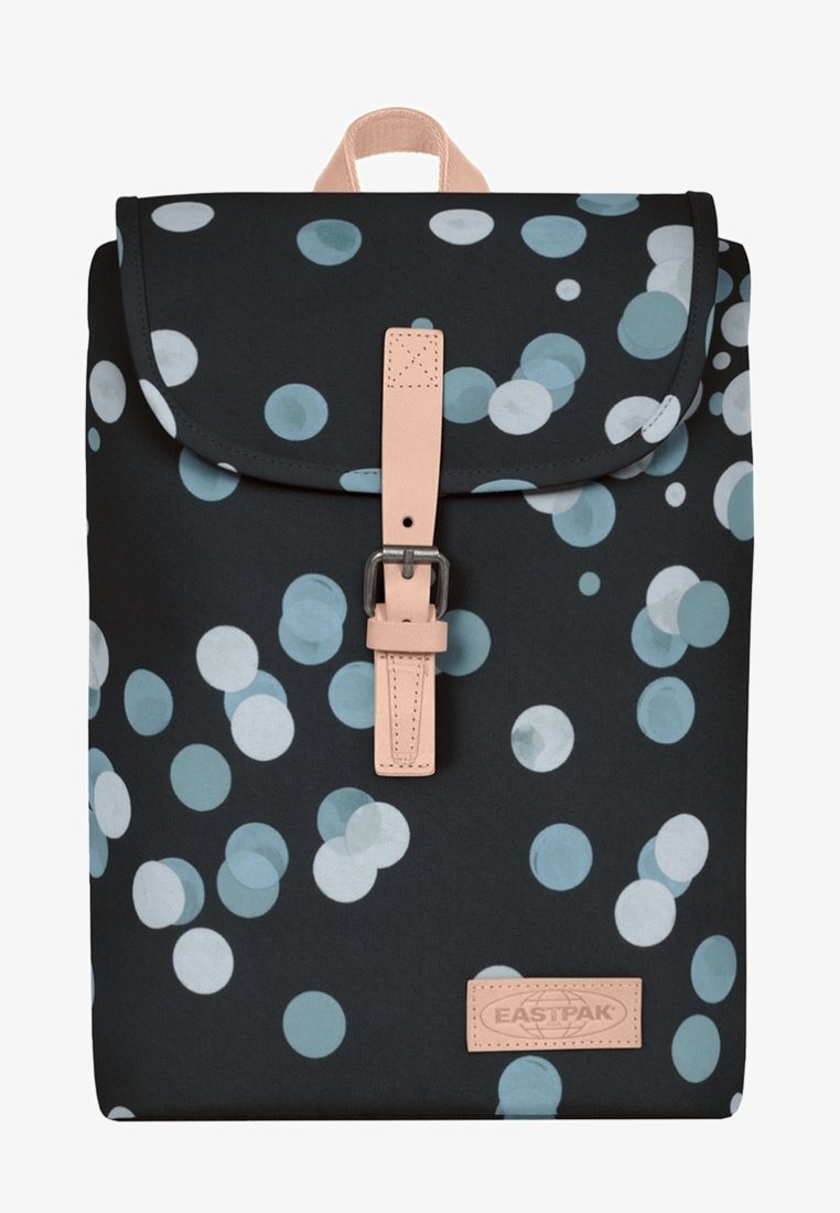 Ryggsäck med svart tyg med ett mönster av ljusblå och vita cirklar, ett beige läderrem och en rektangulär logotypapplikation.