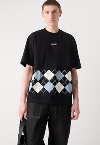 Melnas kokvilnas T-krekls ar īsām piedurknēm, apakšā ar zilu un baltu argyle rakstu un "HUGO" logotipu uz krūts.