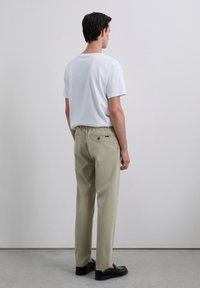 Pantalones de algodón beige claro con un corte holgado, que cuentan con una cinturilla elástica, un bolsillo trasero y se combinan con una camiseta blanca lisa. Zapatos negros tipo slip-on.