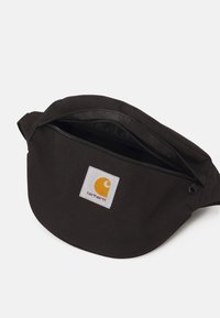 Borsa di stoffa nera con forma arrotondata, dotata di chiusura con zip nella parte superiore e un'etichetta bianca quadrata con un logo giallo.