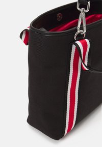 Svart tygväska med en texturerad yta, ett rött foder och ett band med röda, vita och röda r änder. Metalldetaljer är synliga.