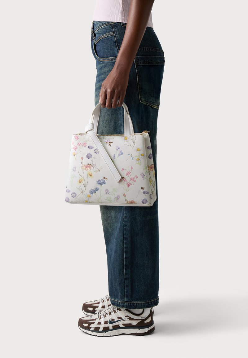 Sac à main à imprimé floral avec une surface texturée blanche, deux anses supérieures et une bandoulière amovible, associé à un jean en denim et des baskets.